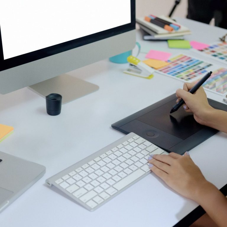 Ein Schreibtisch mit einem Computer, Grafiktablett und bunten Notizen.